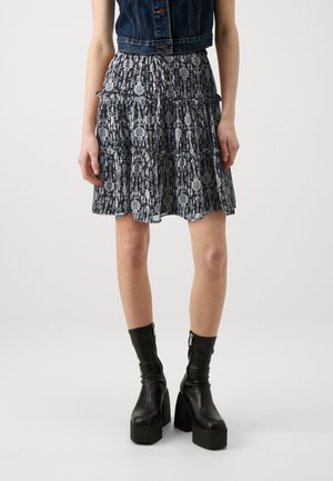Personne portant une jupe noire et blanche à motifs, une veste courte en jean foncé, et des bottines noires à plateforme avec des fermetures éclair.