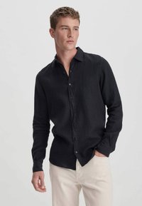 Zwart linnen overhemd met een button-down kraag en lange mouwen, met een ontspannen pasvorm en een gladde textuur, gecombineerd met lichtbeige broek.