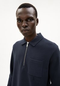 Navy blue zip-up sweatshirt made of textured fabric, featuring a flat collar and a chest pocket with branded detail.