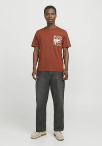 Bordo kratki rukav T-shirt s bijelim grafičkim printom na lijevoj strani džepa, u kombinaciji s crnim širokim trapericama i bež cipelama.