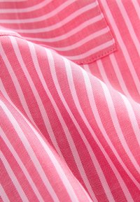 Pink fabric with alternating white and light pink stripes, smooth texture, and a subtle sheen. Includes a small stitched pocket detail.