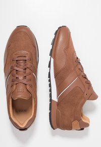 Baskets marron en cuir texturé et daim, avec des lacets foncés, une bande blanche sur la semelle intermédiaire et une semelle extérieure en caoutchouc avec motif de crampons.