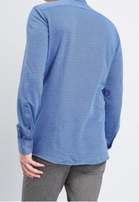 Camicia con motivo blu e finitura testurizzata, maniche lunghe e chiusura a bottone ai polsini, vista da dietro.