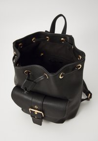 Sac seau en cuir noir avec une finition texturée, œillets dorés et un rabat avant avec fermeture à boucle. L'intérieur est doublé de tissu sombre.
