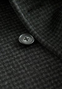 Close-up of a dark gray textured fabric with a single black four-hole button sewn near a folded edge.