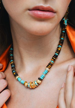 Collier en perles présentant un mélange de noir, turquoise et accents dorés, avec des formes arrondies et cylindriques dans un design en couches.