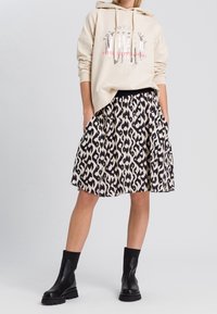 Beige hoodie with graphic print, paired with a black and cream patterned skirt. Black ankle boots complete the look.