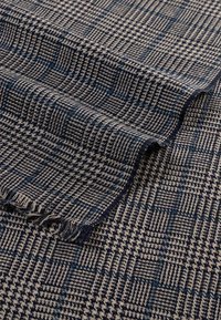 Woven blanket in dark blue and beige houndstooth pattern, featuring fringed edges and a textured finish.