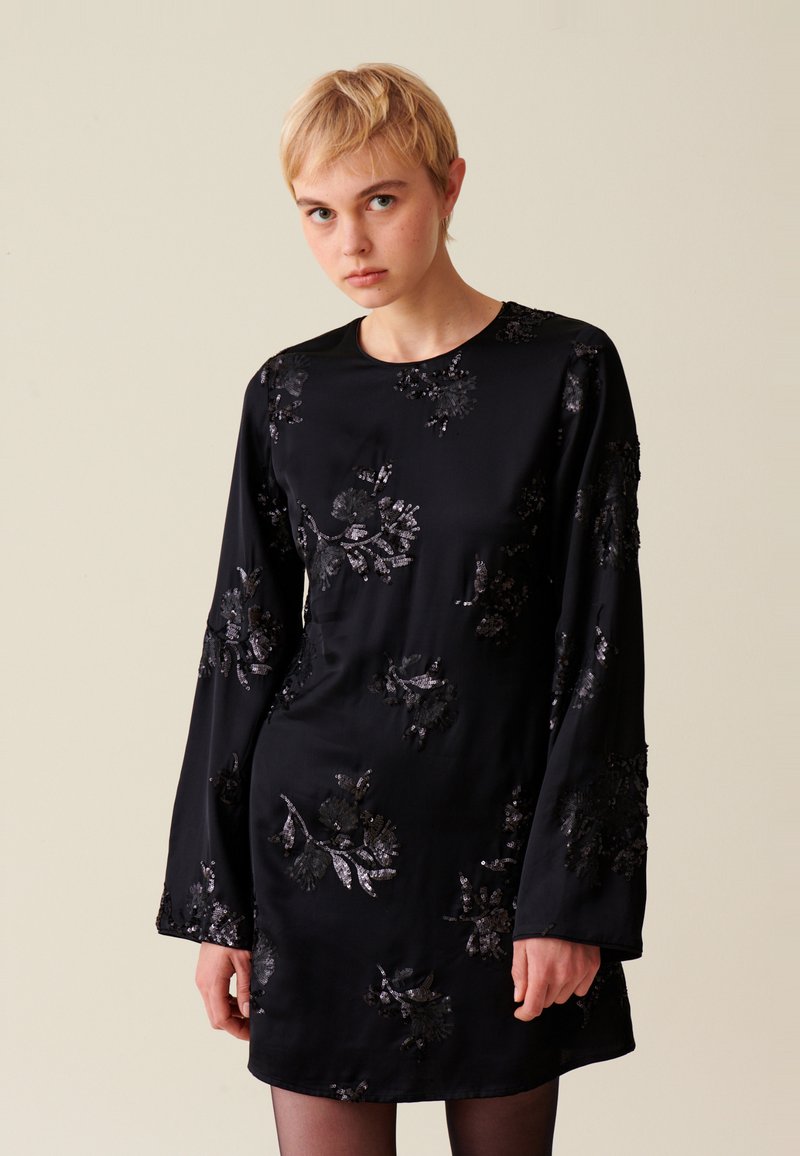 Schwarzes satin langärmliges Kleid mit floralen Paillettenverzierungen. Verfügt über einen runden Halsausschnitt und einen lässigen Schnitt. Glatte Textur, knielang.