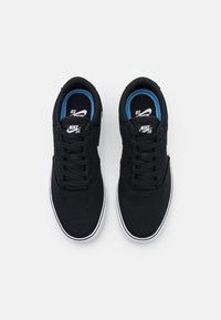 Černé tenisky Nike SB s plátnovým svrškem, bílými detaily a modrým pod šívkou; ploché černé tkaničky, gumové podrážky a minimalistický design.