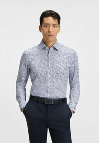 Witte blouse met blauw bloemenpatroon, lange mouwen, met knoopkraag, gecombineerd met donkere broek en een zwarte riem. Gestructureerde stof.