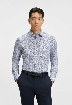 White shirt with blue floral pattern, long sleeves, buttoned collar, paired with dark trousers and a black belt. Textured fabric.