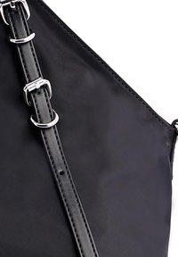 Bolso de mano negro con una superficie lisa y una correa ajustable que presenta hebillas y anillas de plata.