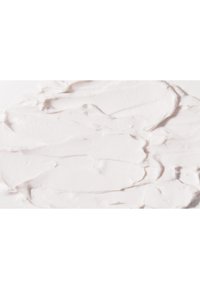 Crème blanche à tartiner avec une texture lisse, montrant une application en couches. La surface présente un éclat brillant avec de subtiles variations d'épaisseur.