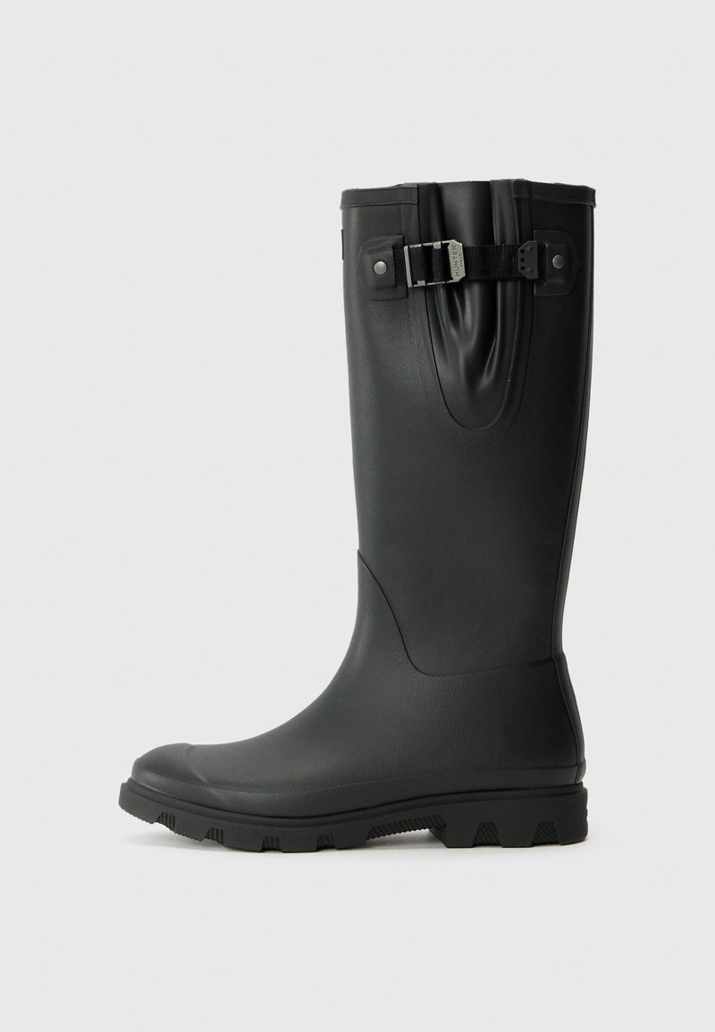 Botte de pluie en caoutchouc noire avec un bout arrondi, une semelle robuste et un détail de boucle décoratif sur le dessus. Texture lisse et hauteur mi-mollet.