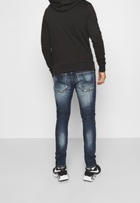 Sudadera gris oscuro combinada con vaqueros ajustados de denim azul, que presentan un ligero desgastado, dos bolsillos traseros y una textura suave, complementados por zapatillas negras.