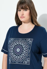 Námořnická modrá tričko s kulatým výstřihem, zdobené velkým, složitým mandalovým vzorem v světle modré a růžové barvě. Měkký bavlněný materiál, krátké rukávy.