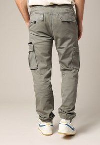 Cargo pants in lichtgrijze stof met taps toelopende boorden, featuring meerdere zakken en een elastische tailleband, gecombineerd met witte sneakers.