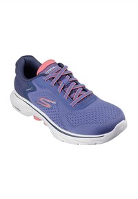 Zapato deportivo morado con parte superior de malla, acentos rosa, suela blanca y patrón de superficie texturizado. Los cordones son visibles. Logo de la marca en el costado.