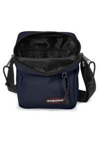 Borsa in tela blu navy con cima con zip, dotata di un ampio interno nero e una tasca esterna con zip. Include una tracolla regolabile con texture.