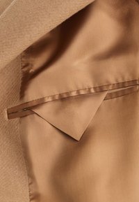 Doublure intérieure en satin lisse couleur beige avec une poche passepoilée intérieure et un rabat assorti en tissu à l'intérieur d'un manteau camel texturé.