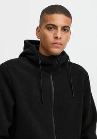 Black fleece hoodie with a zippered front, adjustable drawstrings at the hood, and a smooth texture. Designed for comfort and warmth.