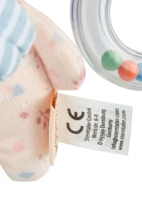 Plush toy in soft pink fabric with blue and pink floral patterns, featuring a textured surface, a CE label, and a circular rattle with colored beads.