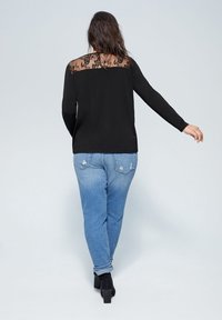 Schwarzes Langarmoberteil mit Spitzenrücken, kombiniert mit hellblauen, distressed Jeans und schwarzen Absatzstiefeln. Schlichtes und klassisches Design.