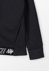 Černá mikina s texturovanou tkaninou, bočními rozparky a kontrastním bílým logem na lemu. Hřebíkované manžety pro zvýšení detailu.