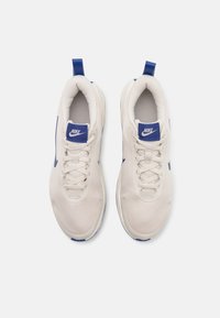Par de zapatillas Nike beige con acentos azules, con cordones visibles y cuellos acolchados, vistas desde arriba sobre un fondo blanco.