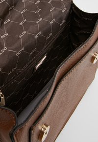 Borsa a mano in pelle marrone con finitura testurizzata e hardware dorato. L'interno presenta una fodera a motivi e una tasca con cerniera.