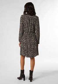 Robe à imprimé zèbre noir et beige avec des manches longues, taille cintrée et tissu léger ; portée avec des bottines noires.