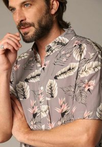 Korte mouwen, blouse met knoopjes en een grijze achtergrond, voorzien van een tropisch blad- en bloemenpatroon in tinten groen, roze en room.