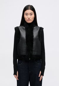 Μαύρο άνετο γιλέκο χωρίς μανίκια, με δερμάτινο μπροστινό μέρος και φουντωτή υφή στο τελείωμα. Υψηλός γιακάς, κλείσιμο με κουμπί και σφιχτή γραμμή.