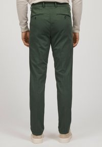 Gröna bomullsbukser med skräddarsydd passform, som har två bakfickor och knäppningar, kombinerat med ljusa skor.