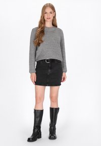 Grijze gebreide trui, zwarte spijkerrok, zwarte laarzen tot de knie. Informele outfit met gestructureerde stof en een getailleerd ontwerp. Zilveren riemaccent.