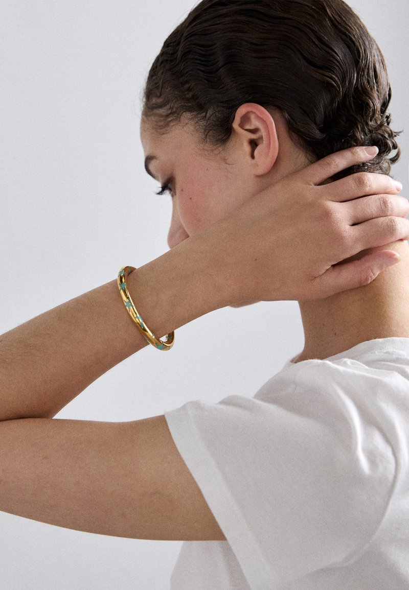 Gold-tone bangle bracelet with turquoise accents, featuring a smooth, rounded design. Worn on a wrist against a plain white background.