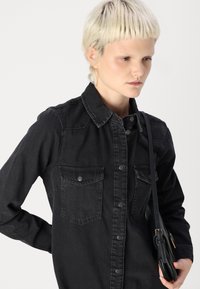 Black denim shirt with a pointed collar, button-down front, and two chest pockets. The fabric has a soft texture, worn look, and a relaxed fit.