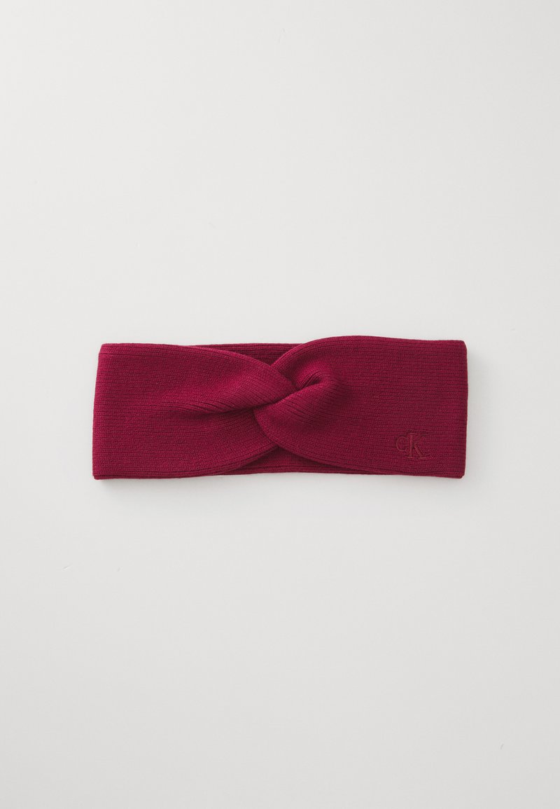 Burgundy knit headband featuring a twisted design at the front and a small embossed logo on the side. Soft texture and wide shape.