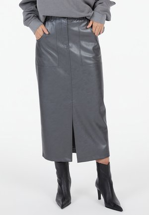 Dunkelgrauer Kunstleder-Midirock mit Frontschlitz und großen Fronttaschen, getragen mit grauem Sweatshirt und schwarzen spitzen Stiefeletten.