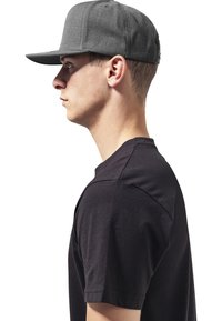 Casquette grise avec une visière plate et un design structuré, portée par une personne en t-shirt noir, présentant des lignes épurées et une texture lisse.