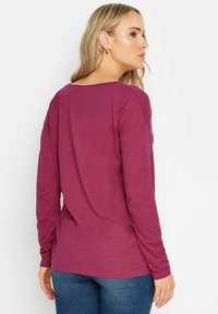 Långärmad skjorta i djup mauve, med en vid halsringning och mjuk textur. Enkel design med en avslappnad passform, kombinerad med blå jeans.