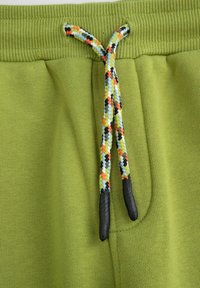 Zielone dresy bawełniane mają ściągacz w pasie oraz multikolorowy sznurek do regulacji z czarnymi końcówkami. Gładka tekstura, prosty design.