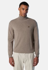 Maglione a collo alto color marrone chiaro realizzato in tessuto morbido. Presenta un design aderente con polsini a coste e un piccolo logo sul petto.