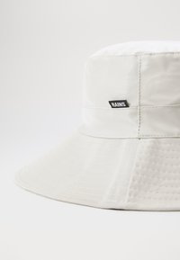 Chapeau seau imperméable blanc avec un large rebord, présentant une surface texturée et une étiquette noire "RAINS" sur le côté.