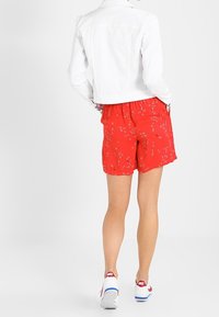 Röda shorts med blommigt mönster och elastisk midja, i kombination med en vit denimjacka. Vita skor med röda detaljer syns också.