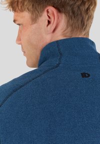Navy blue fleece jacket featuring a high collar, contrasting stitching, and a small black logo on the back. Smooth texture with a fitted design.