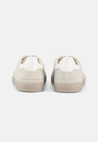 Αθλητικά παπούτσια από σουέντ σε ανοιχτό μπεζ χρώμα με λευκές δερμάτινες λεπτομέρειες. Στρογγυλεμένος πίσω σχεδιασμός και ανάγλυφη εξωτερική σόλα. Μινιμαλιστικό στυλ με διακριτική σήμανση.