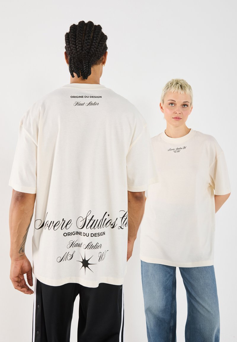 Cream-colored oversized t-shirt in cotton, featuring black printed text on the back and front. Loose fit with short sleeves.
