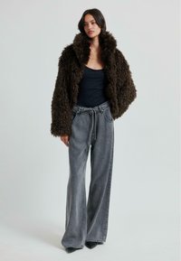 Brun fluffig överdimensionerad jacka med hög krage, svart åtsittande topp och grå vida jeans. Svarta spetsiga klackskor fulländar outfiten.